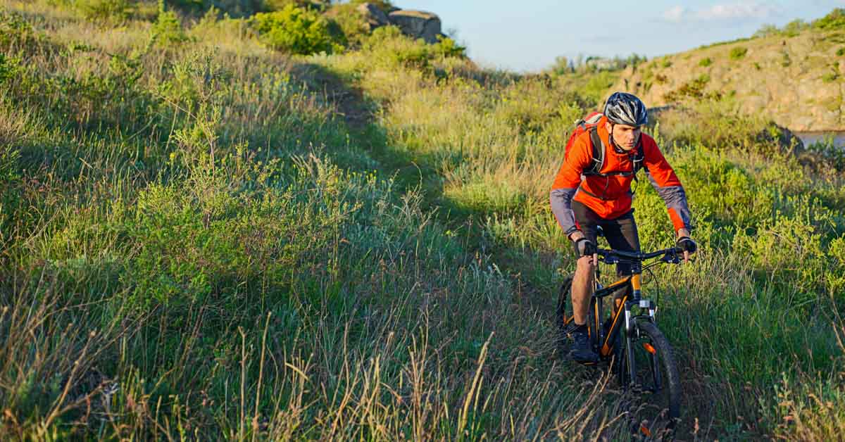 Cyclist In Red Jacket Riding Mountain Bike On The Beautiful Spring Trail. Travel And Adventure Sport Concept