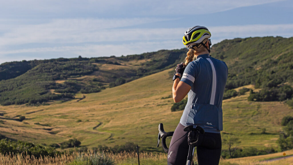 a woman taking a break on a cycling ride overlooking a grassy valley