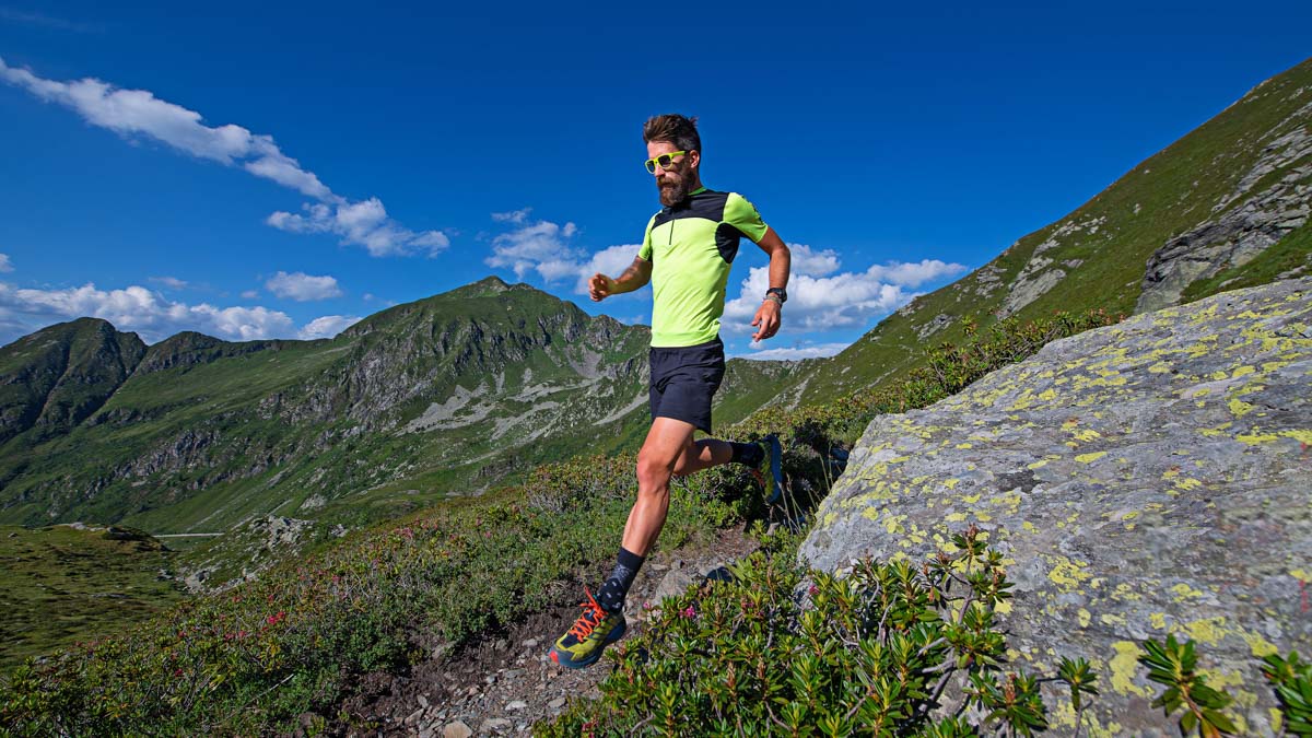 Handsome Bearded Man In Bright Yellow Shirt Trail Running Downhill In The Mountains