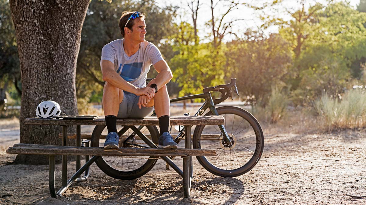 Male Cyclist Sitting On A Bench In The Outdoors Looking Into The Distance