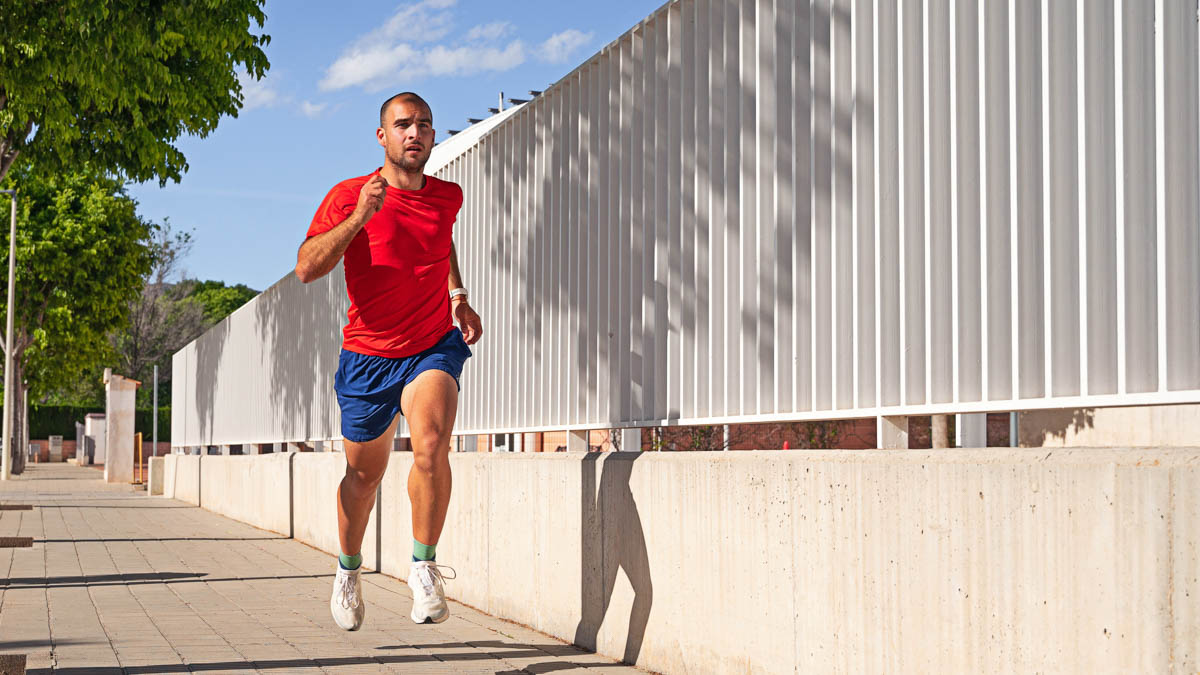 Fit Young Male Runner Doing An Ironman Run Workout Down A City Street Next To A Fence