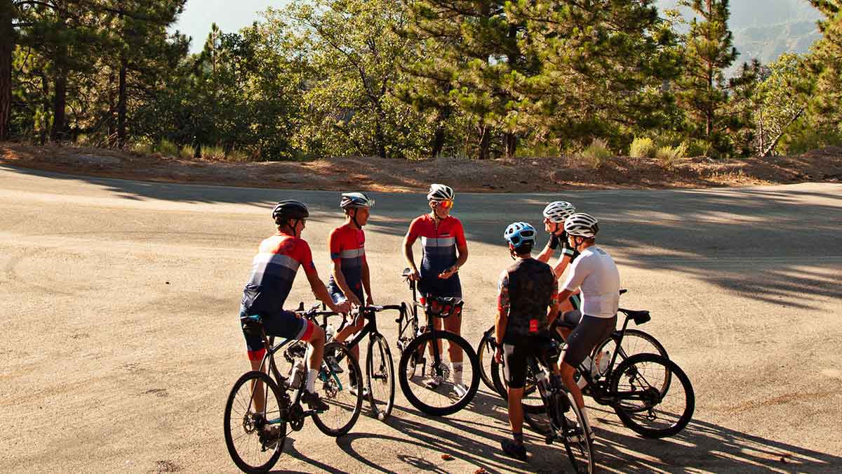 A Group Of Six Cyclists Talking Mid Ride With Their Bikes On A Pullout Of A Road In The Foothills