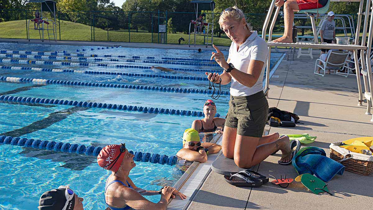 A Female Coach At The Side Of A Swimming Pool Giving Instructions To Several Triathletes Training