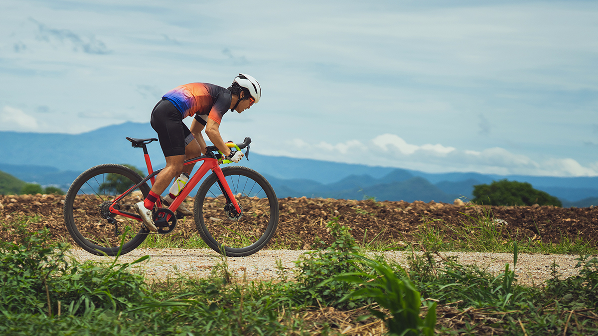 A Cyclist Out Of The Saddle Riding Hard On A Gravel Road In A Tropical Area