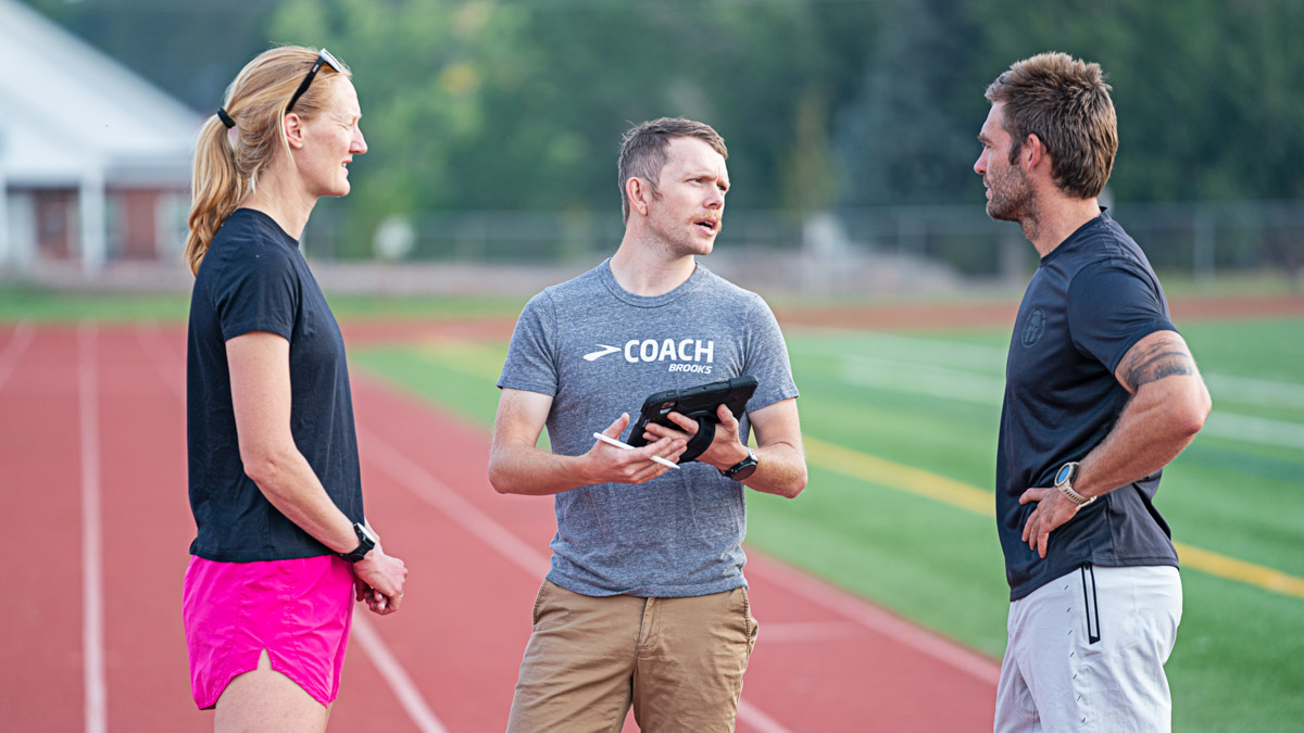 A Male Running Coach Talking With A Woman And Male Runner On A Track