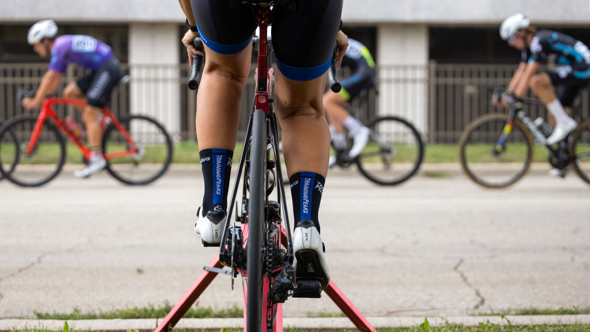 A Cyclist Warming Up On A Trainer Watching A Bike Race From The Curb.