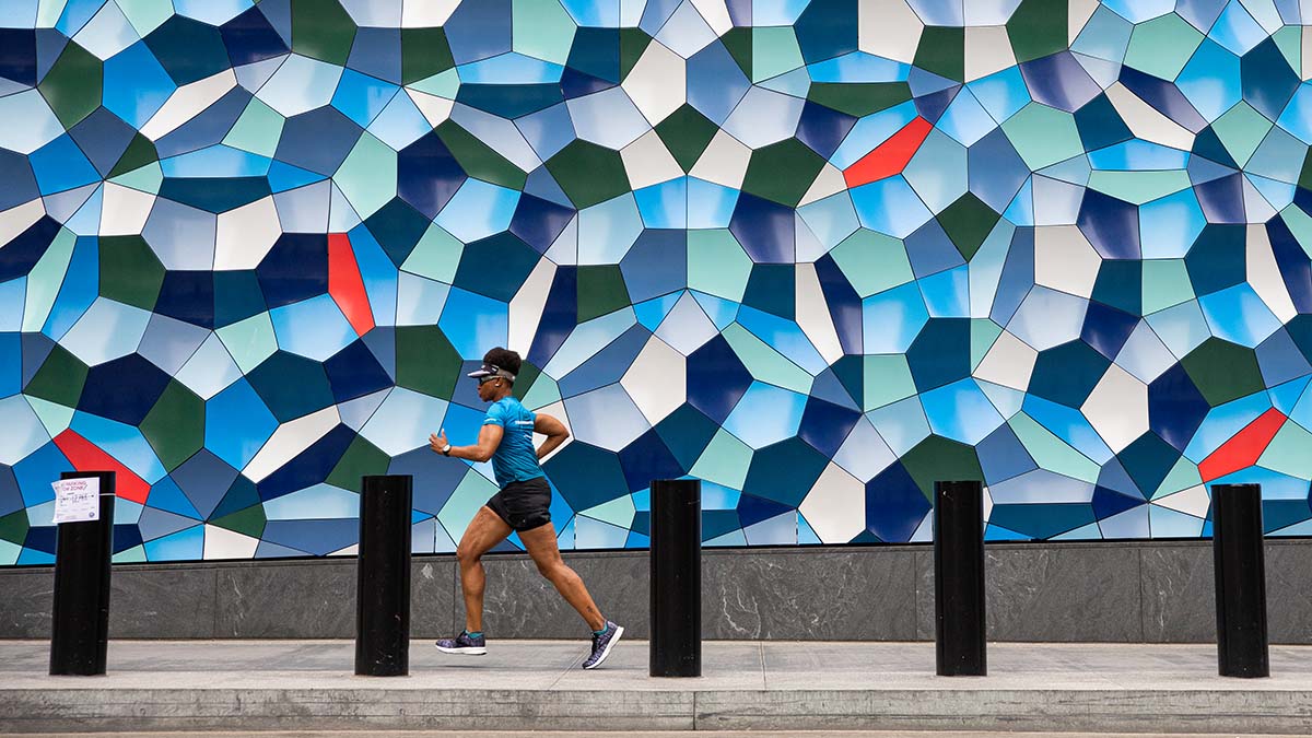 A Woman Running By A Mosaic Wall Of Art In An Urban Setting