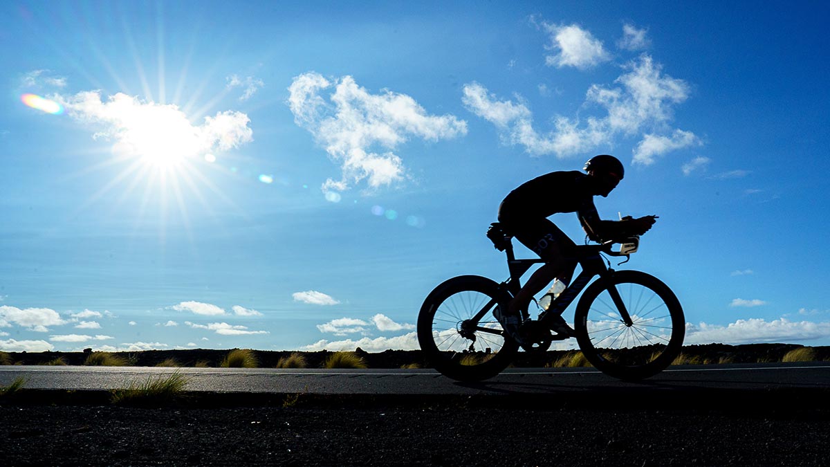 A Triathlete Riding Their Bike On Course At An Ironman As The Sun Shines Down