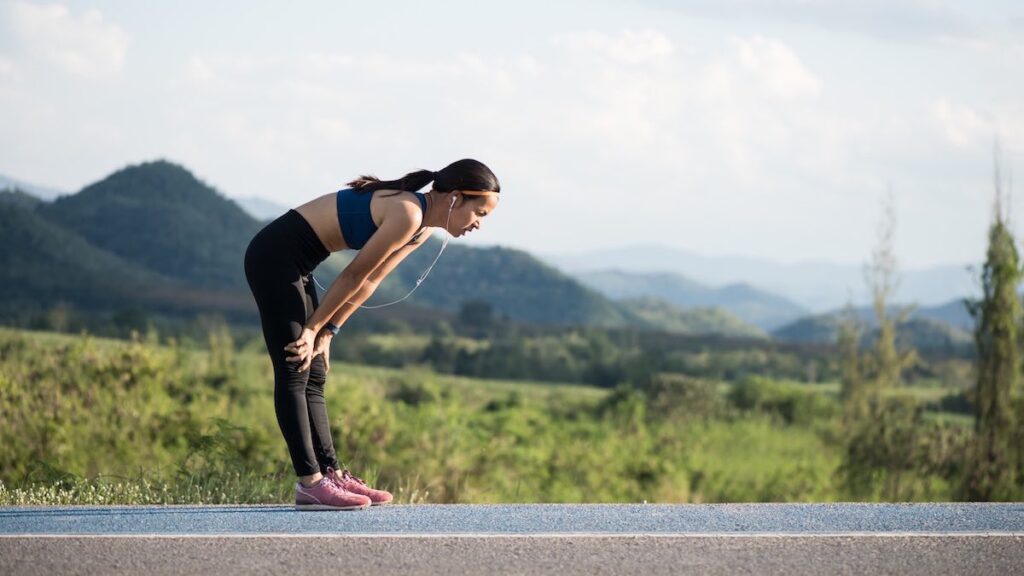 a woman hunched over after running a road with mountains in the background