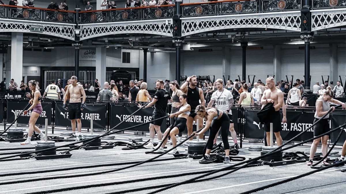 Men And Women Athletes Competing In A Hyrox Competition As People Watch From A Balcony