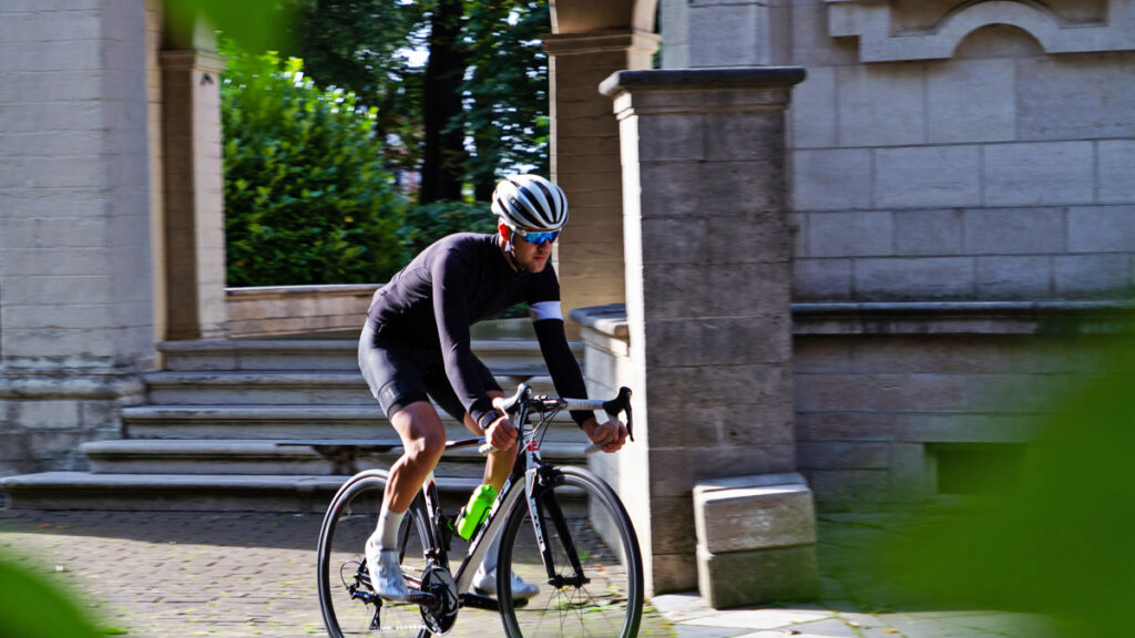 a male cyclist riding his bike through a park with a stairway behind him