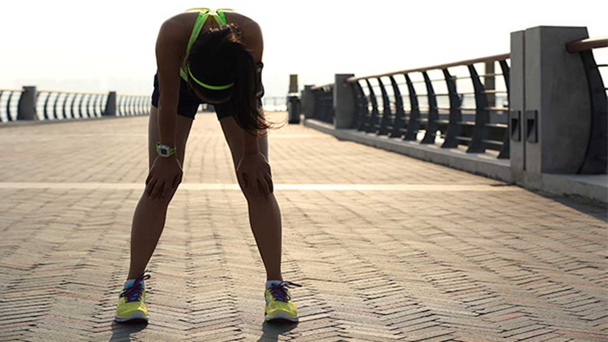 A Female Runner Bent Over With Hands On Her Knees On A Seaside Path