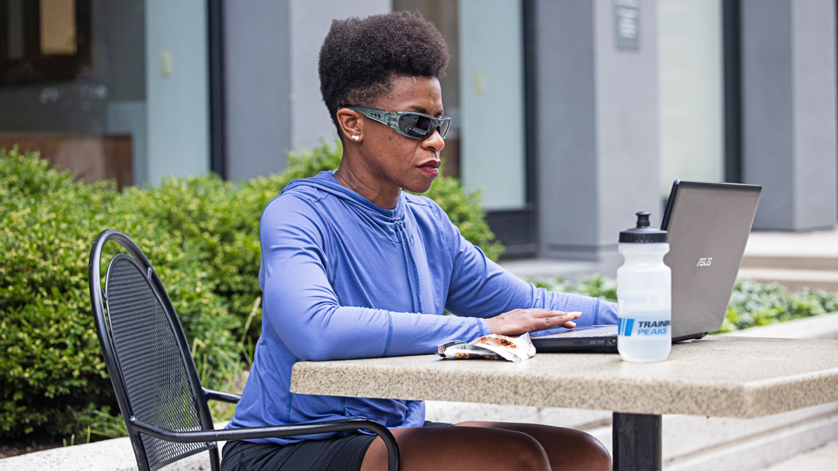 A Woman At A Table Outside Working On A Computer Analyzing Trainingpeaks Files.