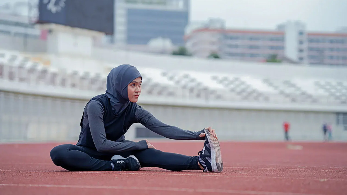 Female Muslim Athlete Stretching On The Track As She Trains And Exercises Through Ramadan