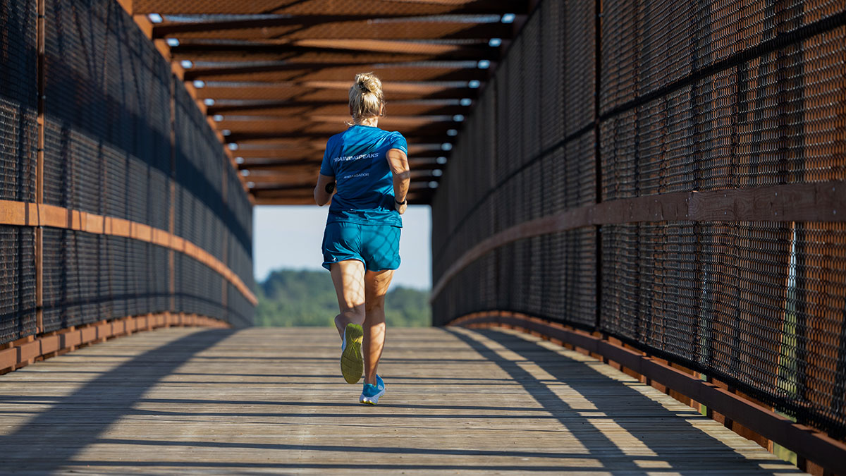 A Woman Running Across A Pedestrian Bridge In The Early Morning As Shadows And Lines Of The Bridge Converge