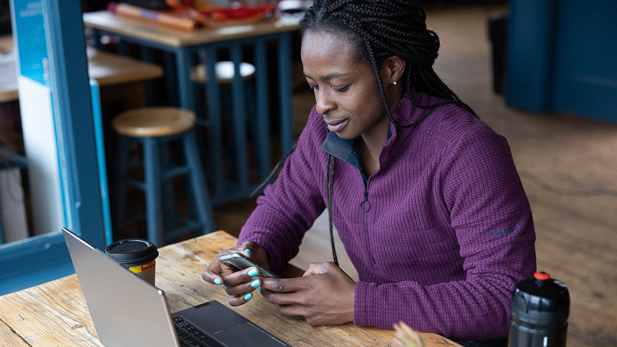 A Woman Working On Her Mobile Phone And Laptop In A Cafe