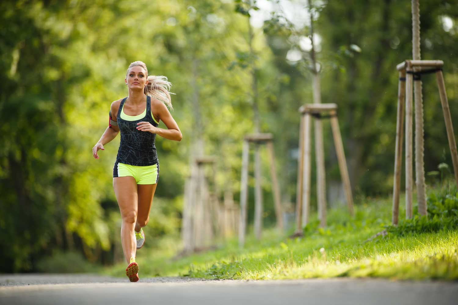 Female Runner Running Along Trail In The Summer With Trees In The Background