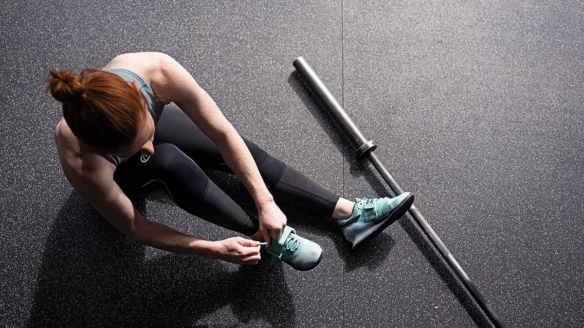 Female Weightlifter Tying Shoes Preparing For A Strength Training Workout