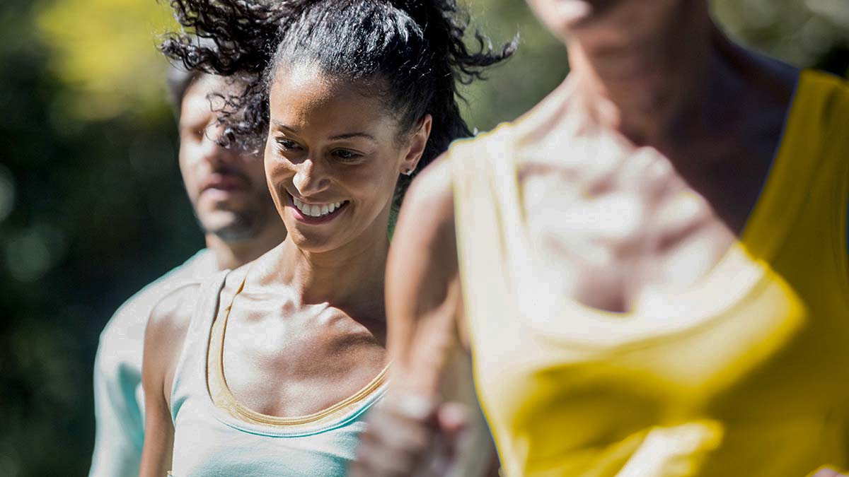 A Woman Runner Smiling With Two Others Surrounding Her On A Sunny Day