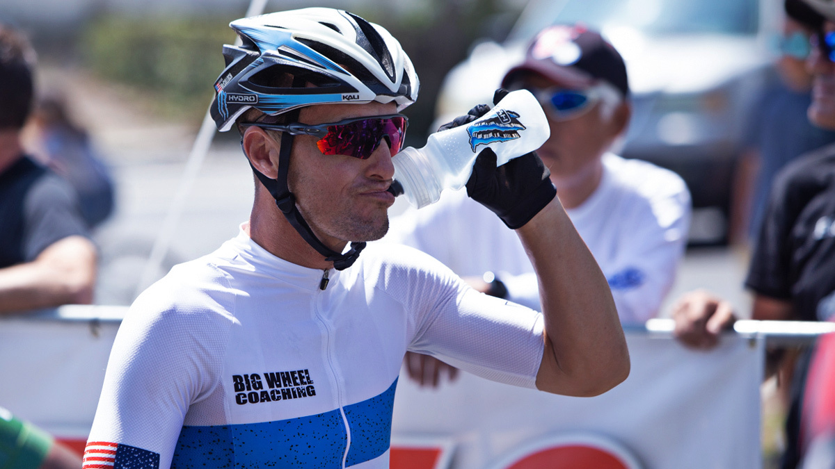 Triathlete Wearing Helmet And Sunglasses At Start Of Racing Drinking Electrolytes Out Of Water Bottle And Staying Hydrated