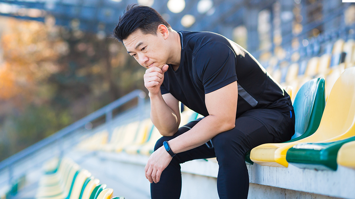 A Male Athlete Sitting On A Seat In A Stadium With His Chin In His Hand Contemplating