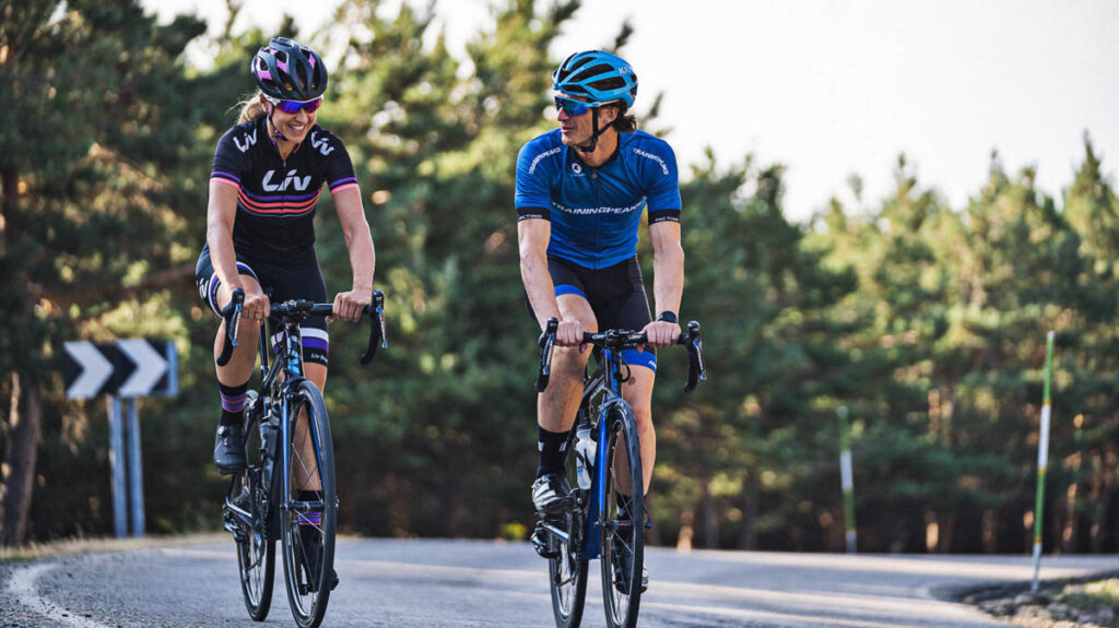 a male cycling coach riding with a female athlete on a road